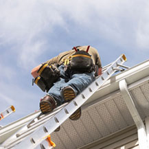 Man on ladder installing eavestroughs on roof